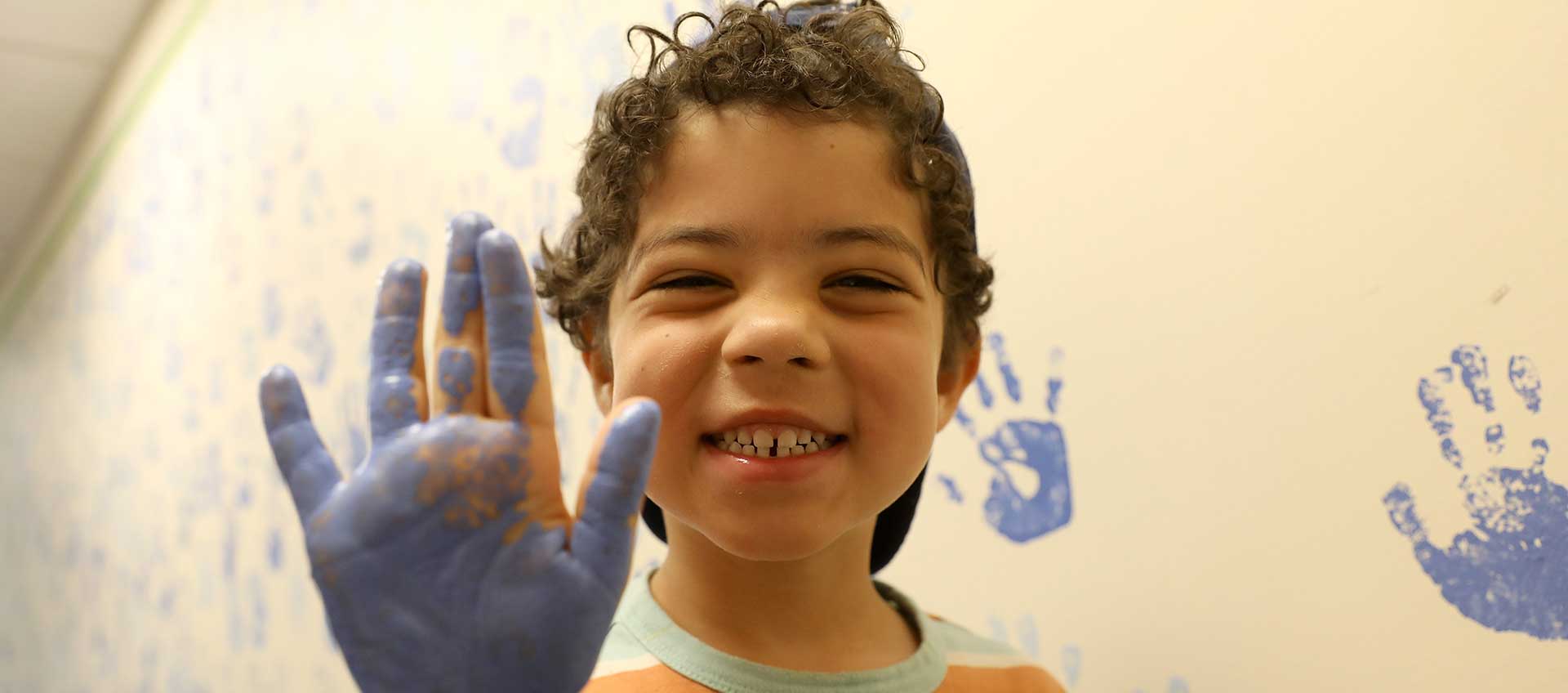 A young student with blue paint on his palm before he adds a handprint to our community wall